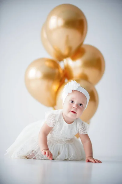 Une petite fille d'un an assise avec un tas de ballons dorés . — Photo