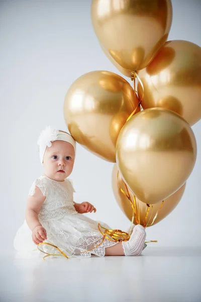 Une petite fille d'un an assise avec un tas de ballons dorés . — Photo