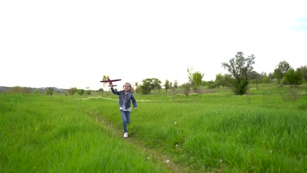 Holčička vypouští do vzduchu ve venkovním parku letadýlko. Dítě odpálí malé letadýlko. Krásná holčička běží na trávě a uvádí na trh růžové hračky letadlo — Stock video