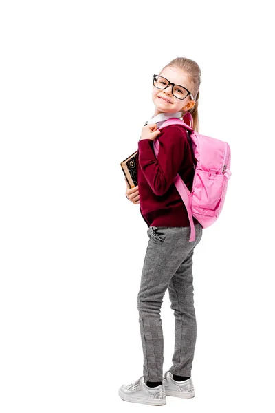 Niño con mochila. Chica en camisa blanca y pantalones grises, gafas redondeadas, sostener un libro, bolso de la escuela y posando como modelo. Aislado sobre blanco — Foto de Stock