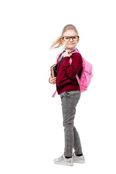 Παιδί με σχολική τσάντα. Κορίτσι σε λευκό πουκάμισο και γκρι παντελόνι, στρογγυλά γυαλιά, κρατήστε ένα βιβλίο, σχολική τσάντα και να θέτουν σαν μοντέλο. Απομονωμένα σε λευκό — Φωτογραφία Αρχείου
