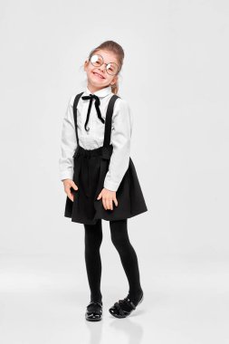 Çekici, sevimli, çekici, utangaç, üniformalı, yuvarlak gözlüklü bir kızın boy boy görüntüsü. Gri arkaplan üzerinde izole