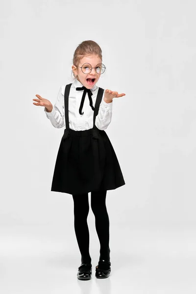 Дивовижна дівчина в шкільній формі, круглі окуляри розтягують руки на сторони обурені. Студійний знімок. Ізольований сірий фон — стокове фото