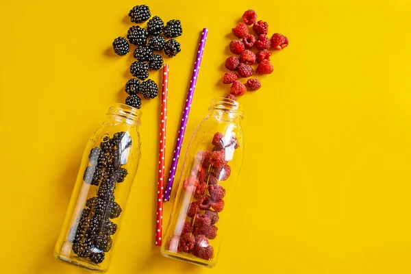 Blackberry and raspberry fruit in glass bottles with straws on yellow background. Fresh organic Smoothie ingredients. Superfoods and health or detox diet food concept. — ストック写真