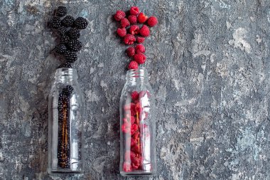 Blackberry and raspberry fruit in glass bottles with straws on stone background. Fresh organic Smoothie ingredients. Superfoods and health or detox diet food concept