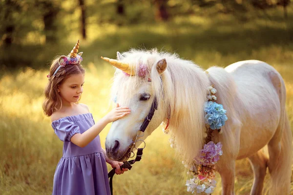 女孩在紫色礼服与独角兽的花环在头发拥抱和亲吻白色独角兽。梦想成真。童话 — 图库照片