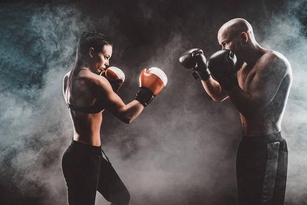 Mujer sin camisa haciendo ejercicio con entrenador en el boxeo y autodefensa lección, estudio, humo de fondo. Lucha femenina y masculina — Foto de Stock