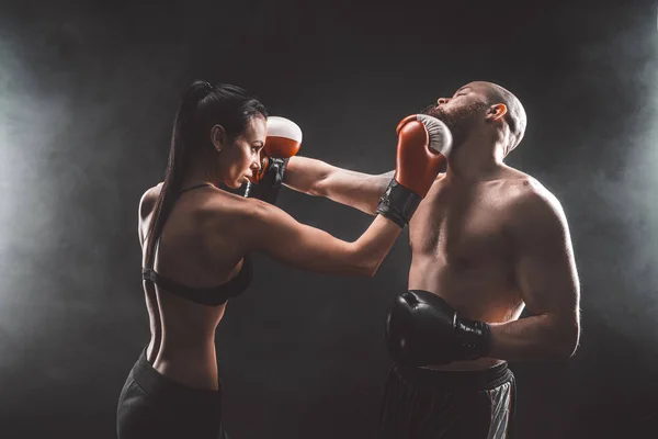 Shirtless Woman exercitando-se com o treinador na aula de boxe e autodefesa, estúdio, fumaça no fundo. Feminino e masculino luta — Fotografia de Stock