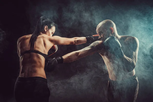 Mujer sin camisa haciendo ejercicio con entrenador en el boxeo y autodefensa lección, estudio, humo de fondo. Lucha femenina y masculina — Foto de Stock