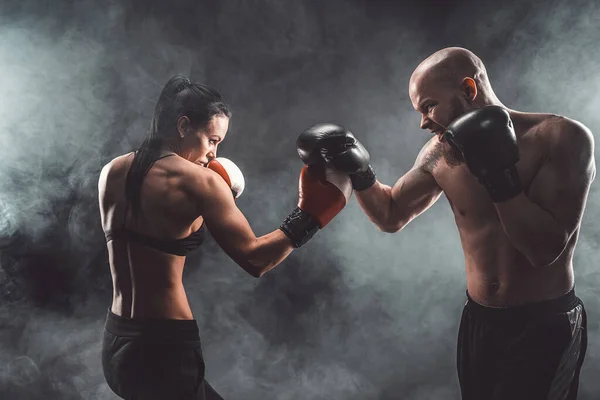Shirtless Woman traint met trainer bij boks- en zelfverdedigingsles, studio, rook op de achtergrond. Vrouwelijke en mannelijke strijd — Stockfoto