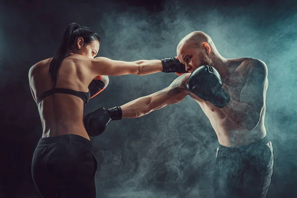 Mujer sin camisa haciendo ejercicio con entrenador en el boxeo y autodefensa lección, estudio, humo de fondo. Lucha femenina y masculina — Foto de Stock