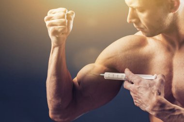 Vücut geliştirici vitamin enjeksiyonu yapar. Siyah arka planda mükemmel fiziği olan sporcu bir adamın fotoğrafı. Kuvvet ve motivasyon