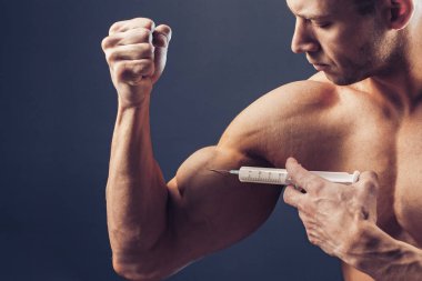 Vücut geliştirici vitamin enjeksiyonu yapar. Siyah arka planda mükemmel fiziği olan sporcu bir adamın fotoğrafı. Kuvvet ve motivasyon