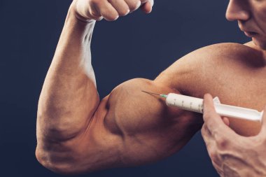 Vücut geliştirici vitamin enjeksiyonu yapar. Siyah arka planda mükemmel fiziği olan sporcu bir adamın fotoğrafı. Kuvvet ve motivasyon