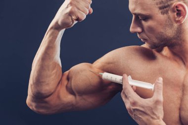 Vücut geliştirici vitamin enjeksiyonu yapar. Siyah arka planda mükemmel fiziği olan sporcu bir adamın fotoğrafı. Kuvvet ve motivasyon
