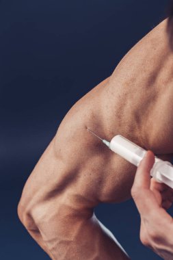 Vücut geliştirici vitamin enjeksiyonu yapar. Siyah arka planda mükemmel fiziği olan sporcu bir adamın fotoğrafı. Kuvvet ve motivasyon