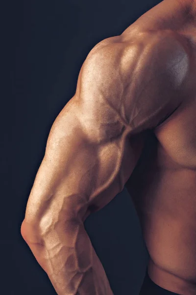 Fitness hombre fondo hombro bíceps músculos pectorales tríceps culturista sobre un fondo oscuro demuestra la forma física para las clases en el gimnasio — Foto de Stock