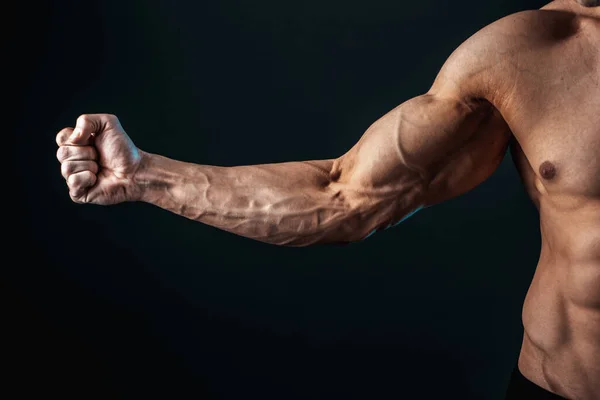 Gespannen arm geklemd in vuist, aderen, bodybuilder spieren op een donkere achtergrond, isoleren — Stockfoto