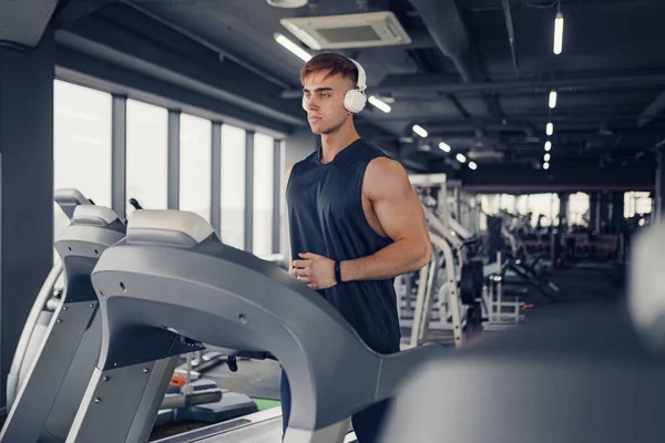 Modern spor salonunda panoramik pencereli koşu bandında koşarken kulaklıkla müzik dinleyen konsantre zinde bir adam.. — Stok fotoğraf