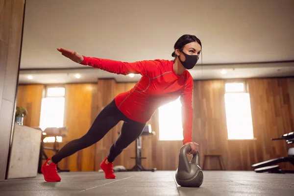 Coronavirus的运动女孩在面具里做Kettlebells Planking — 图库照片