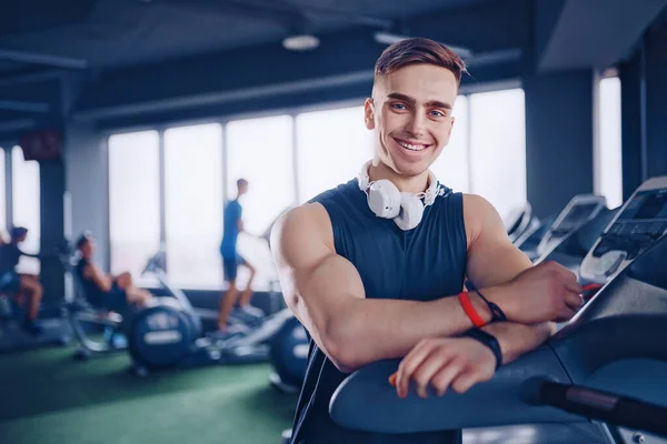 Spor salonunda koşu bandının yanında kollarını kavuşturmuş kendine güveni tam bir erkek eğitmen. — Stok fotoğraf