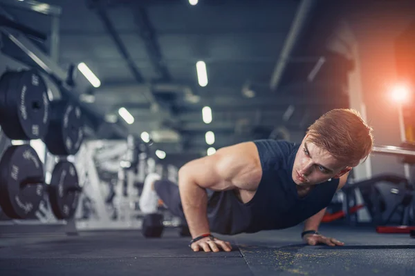 Un joven atlético haciendo flexiones en el gimnasio. Musculoso y fuerte chico haciendo ejercicio. — Foto de Stock