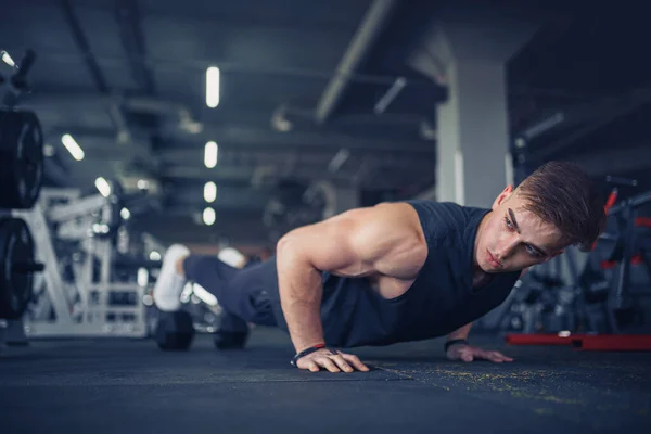 Een jonge atleet die push-ups doet in de sportschool. Gespierde en sterke man oefenen. — Stockfoto