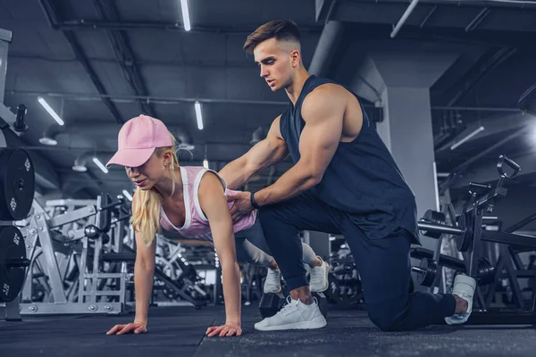 Fitness instructor help girl to do push ups on training in fitness center — Stock Photo, Image