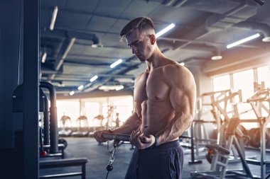 Kas geliştirme vücut geliştiricisi, spor salonunda kablolu TV ile makina üzerinde bisiklet egzersizi yapıyor.