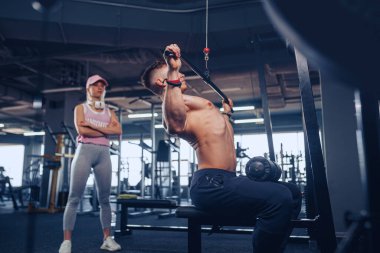 Genç erkek vücut geliştirici kız arkadaşı onu izlerken ağır ağırlık egzersizi yapıyor.