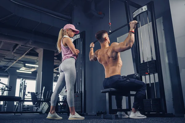 Young male bodybuilder doing heavy weight exercise while his girlfriend watching him — Stock Photo, Image