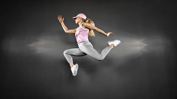 Νεαρή γυναίκα με γυμνασμένο σώμα πηδάει και τρέχει πάνω σε γκρι φόντο. Θηλυκό μοντέλο στην άσκηση αθλητικών ειδών — Φωτογραφία Αρχείου