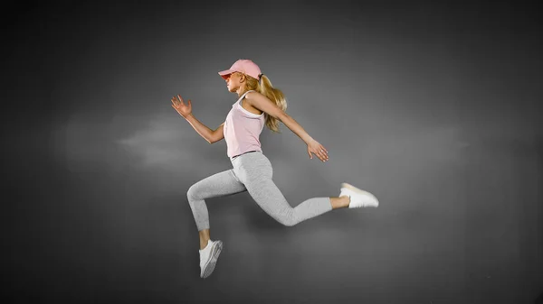 Молодая женщина с подходящим телом прыгает и бежит на сером фоне. Женская модель в спортивной одежде — стоковое фото