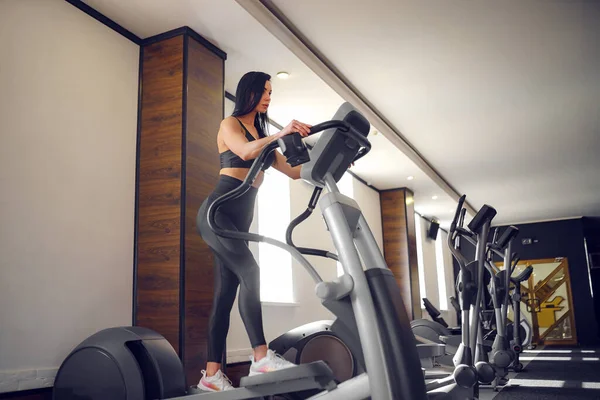 Entrenamiento en el gimnasio Fitness girl coach trabajando en Step machine y mostrando su figura posando en un traje deportivo —  Fotos de Stock