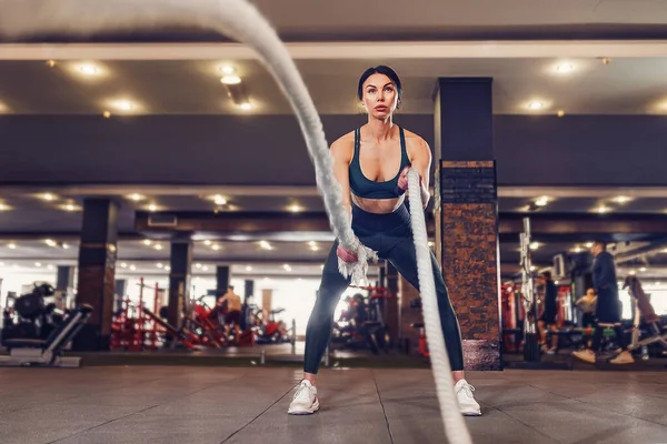 Caucásico en forma mujer vestida en sportsoutfit posando con cuerdas de batalla en el gimnasio — Foto de Stock