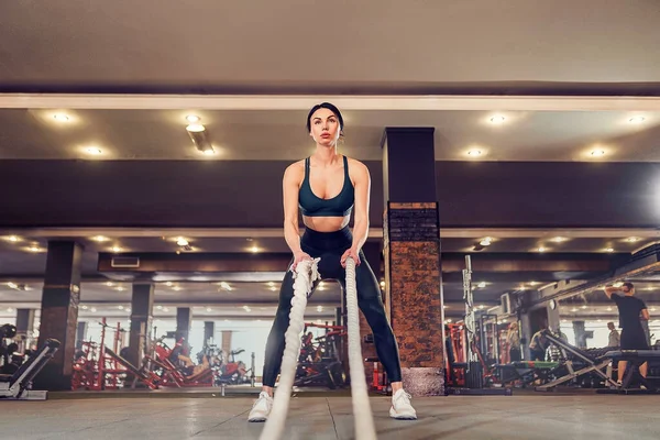 Caucásico en forma mujer vestida en sportsoutfit posando con cuerdas de batalla en el gimnasio — Foto de Stock