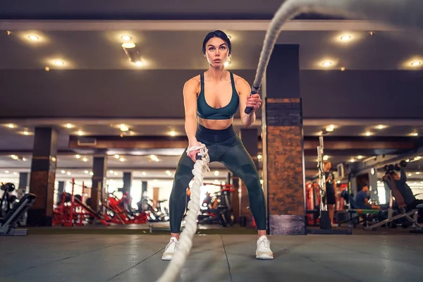 Caucásico en forma mujer vestida en sportsoutfit posando con cuerdas de batalla en el gimnasio — Foto de Stock