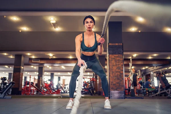 Caucásico en forma mujer vestida en sportsoutfit posando con cuerdas de batalla en el gimnasio — Foto de Stock