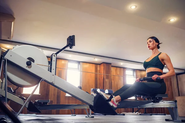 Entschlossene junge Frau trainiert auf Rudergerät im Fitnessstudio — Stockfoto
