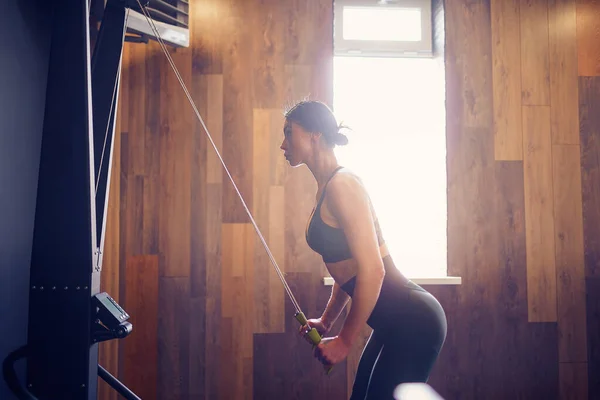 Vastberaden jonge vrouw uit te werken op rij machine in fitness studio — Stockfoto