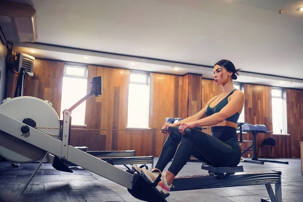 Determined young woman working out on row machine in fitness studio
