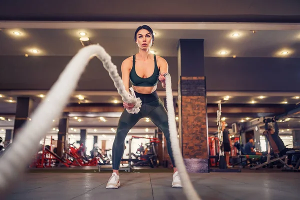 Caucásico en forma mujer vestida en sportsoutfit posando con cuerdas de batalla en el gimnasio — Foto de Stock