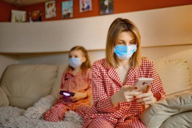 Küçük çocuklu bir kadın evde karantina otomobil karantinasında yüz maskesi takıyor ve COVID-19 hakkında bilgi okuyor.