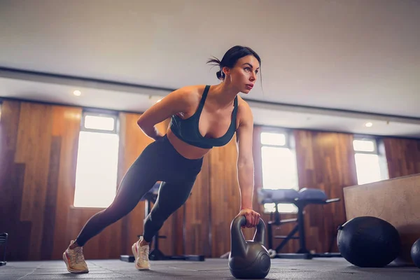 Joven chica motivada haciendo ejercicio de tablón usando pesas con una mano en el gimnasio, foto de cuerpo entero, espacio para copiar — Foto de Stock