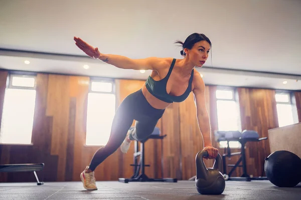 Joven chica motivada haciendo ejercicio de tablón usando pesas con una mano en el gimnasio, foto de cuerpo entero, espacio para copiar — Foto de Stock