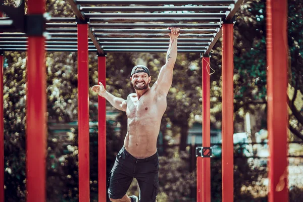 Baard bodybuilder man oefenen op aap bars voor het bovenlichaam in een moderne calisthenics park buiten op een zonnige dag — Stockfoto