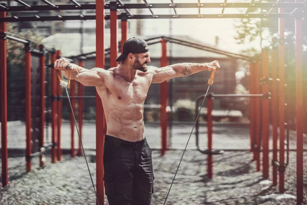 Fitness-Mann trainiert mit Stretchband im Outdoor-Fitnessstudio. — Stockfoto