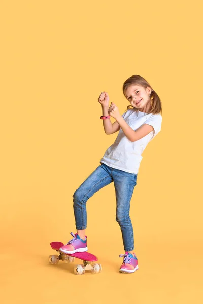 Elegante chica divertida con camiseta blanca, vaqueros azules y zapatillas de deporte, de pie en el monopatín sobre fondo amarillo — Foto de Stock