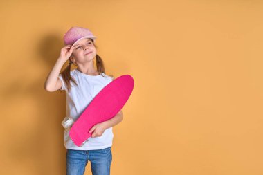 Aktif ve mutlu. Çocuk para tahtasıyla eğleniyor. Gülen yüzlü çocuk kaykay yapıyor. Kızlar için kaykay kaykayı. Hadi gidelim. Sarı arka planda kız bisikleti. Yaz tatili