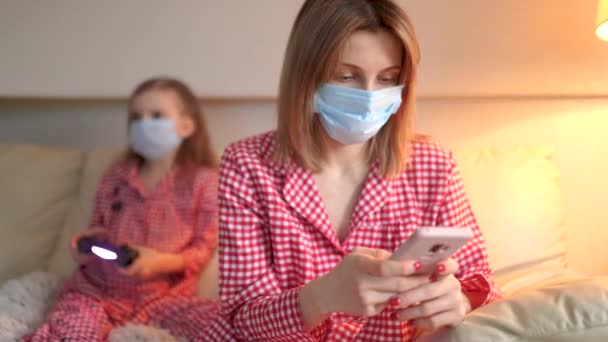 Woman with Little kid at home isolation auto quarantine wearing face mask with smart phone for reading information about COVID-19 — Stock Video